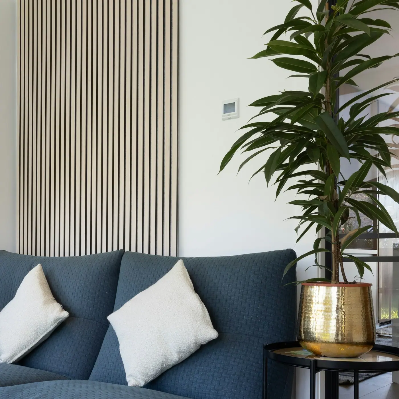 Sala de una casa habitada con lambrín de madera, sillón azul y un control de clima en la pared