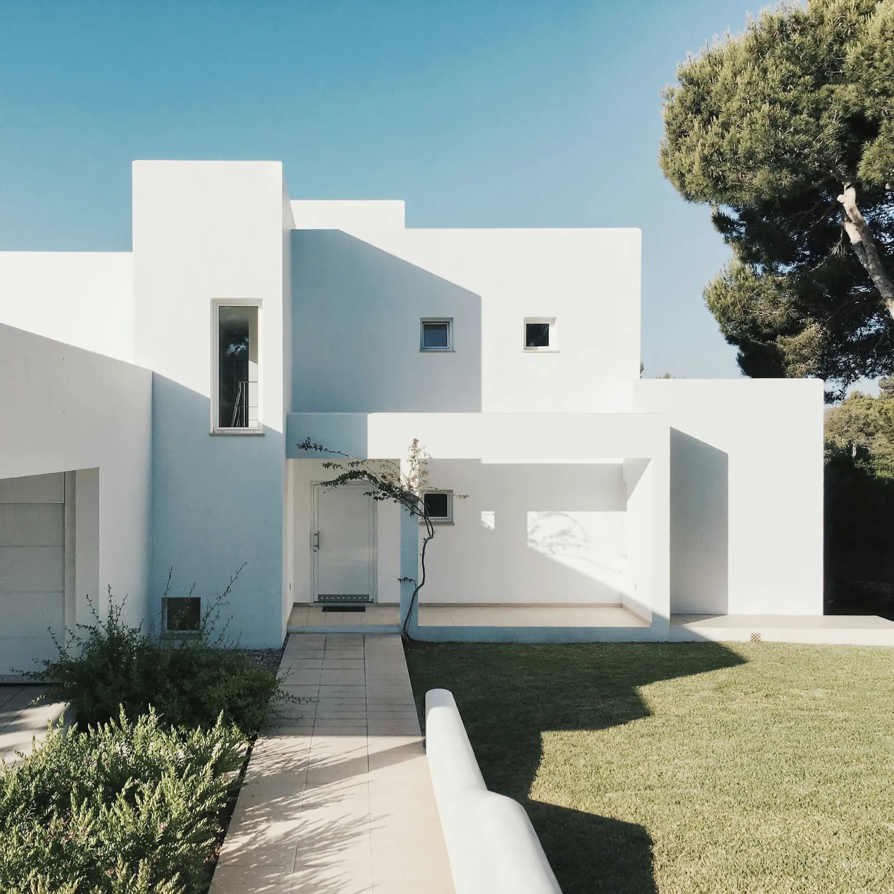Casa moderna de fachada blanca con jardín, entrada con pórtico y luz de la tarde